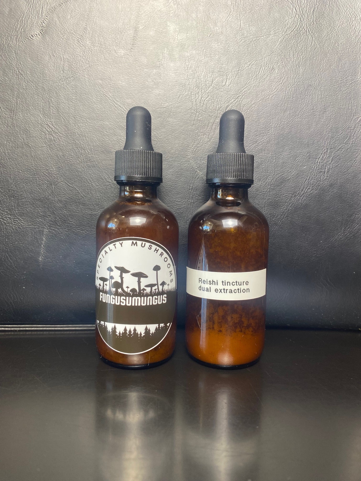 Two bottles of Reishi dual extracted tincture with dropper caps, displayed against a dark background.